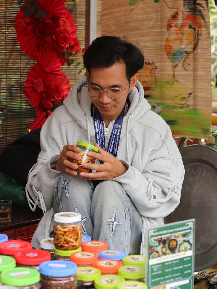 Young man carefully examines a jar at a colorful outdoor market with various jars and decorations around.