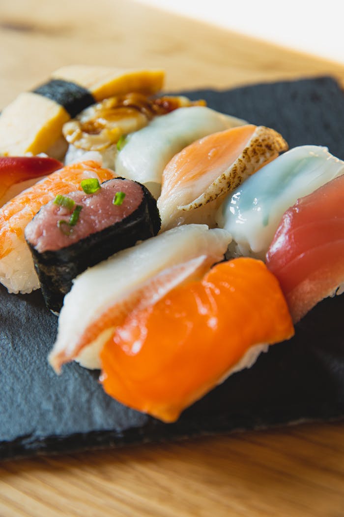 From above of nigiri sushi with different toppings of raw fish served on black slate plate